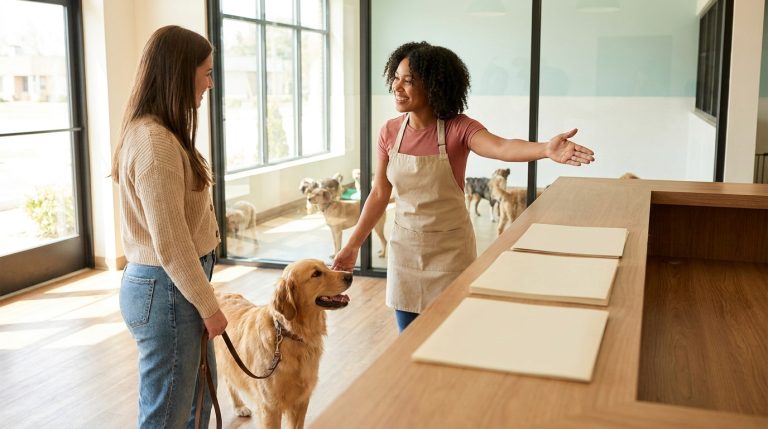 Dog daycare staff member welcoming a pet owner and dog at a clean facility reception desk.
